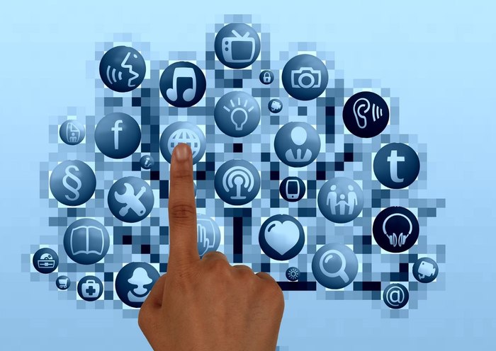 Prst se dotika digitalnega oblaka različnih ikon aplikacij na modri podlagi, kar simbolizira interaktivnost in tehnologijo.